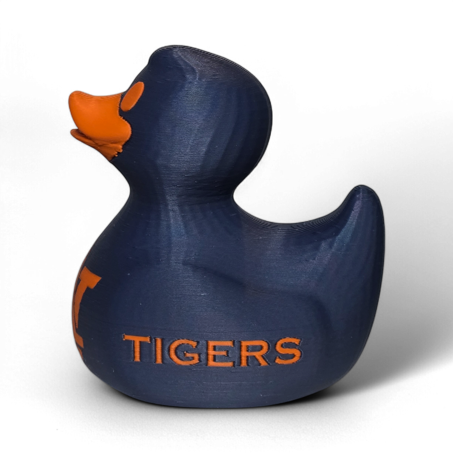 A small 3D printed PLA duck figurine in navy blue with orange accents, featuring the letters 'UA' and the word 'TIGERS' on the front, photographed on a light gray background.