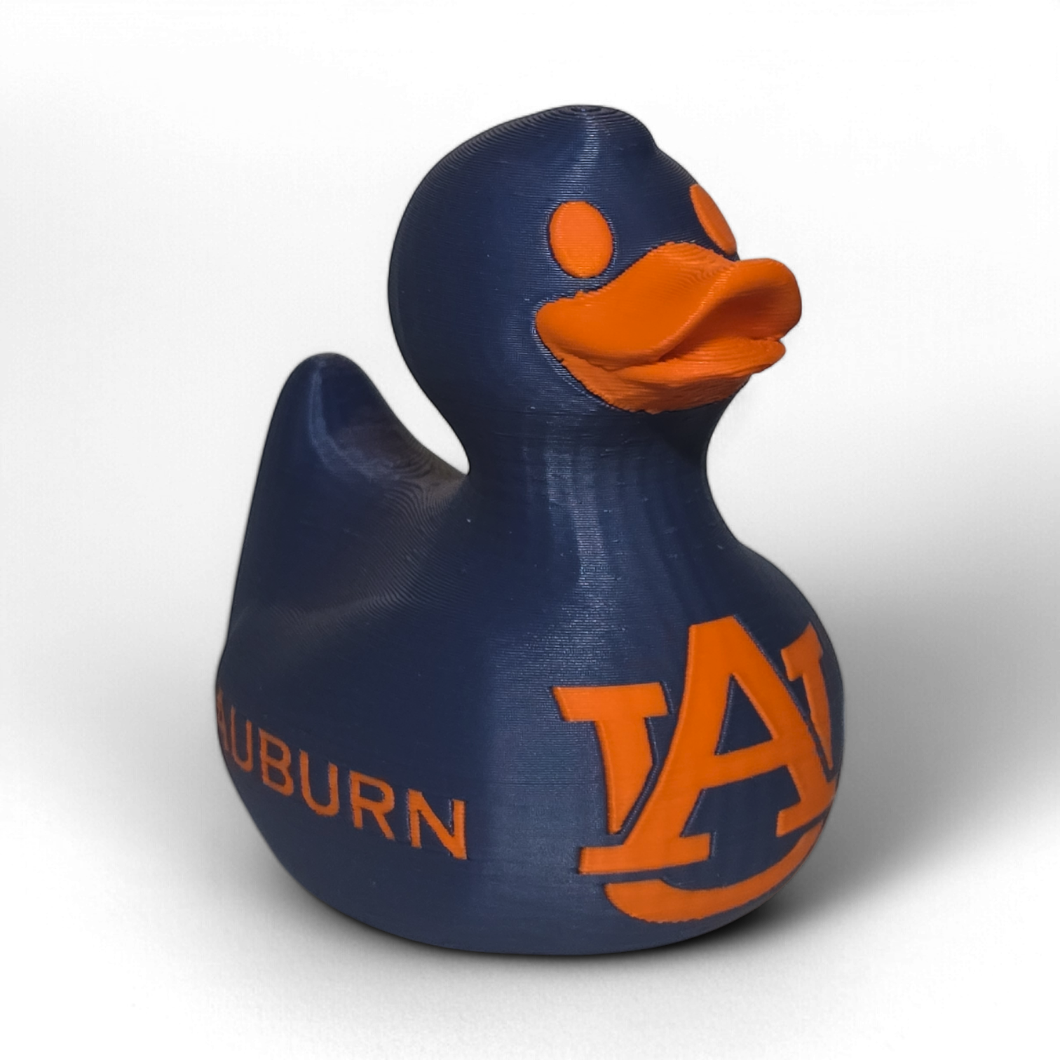 A small 3D printed PLA duck figurine in navy blue with orange accents, featuring the letters 'UA' and the word 'TIGERS' on the front, photographed on a light gray background.