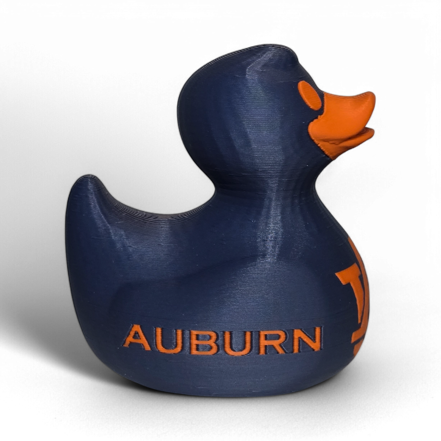 A small 3D printed PLA duck figurine in navy blue with orange accents, featuring the letters 'UA' and the word 'TIGERS' on the front, photographed on a light gray background.