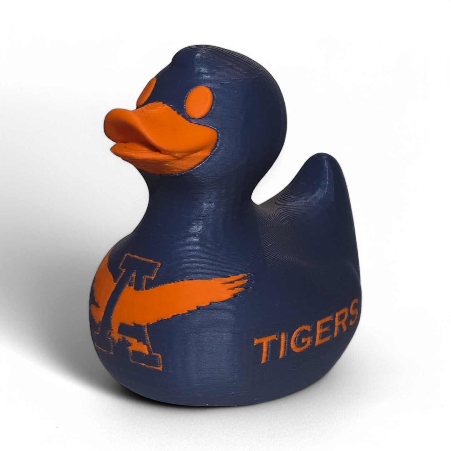 A small 3D printed PLA duck figurine in navy blue with orange accents, featuring the letters 'UA' and the word 'TIGERS' on the front, photographed on a light gray background.