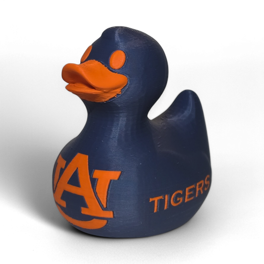 A small 3D printed PLA duck figurine in navy blue with orange accents, featuring the letters 'UA' and the word 'TIGERS' on the front, photographed on a light gray background.