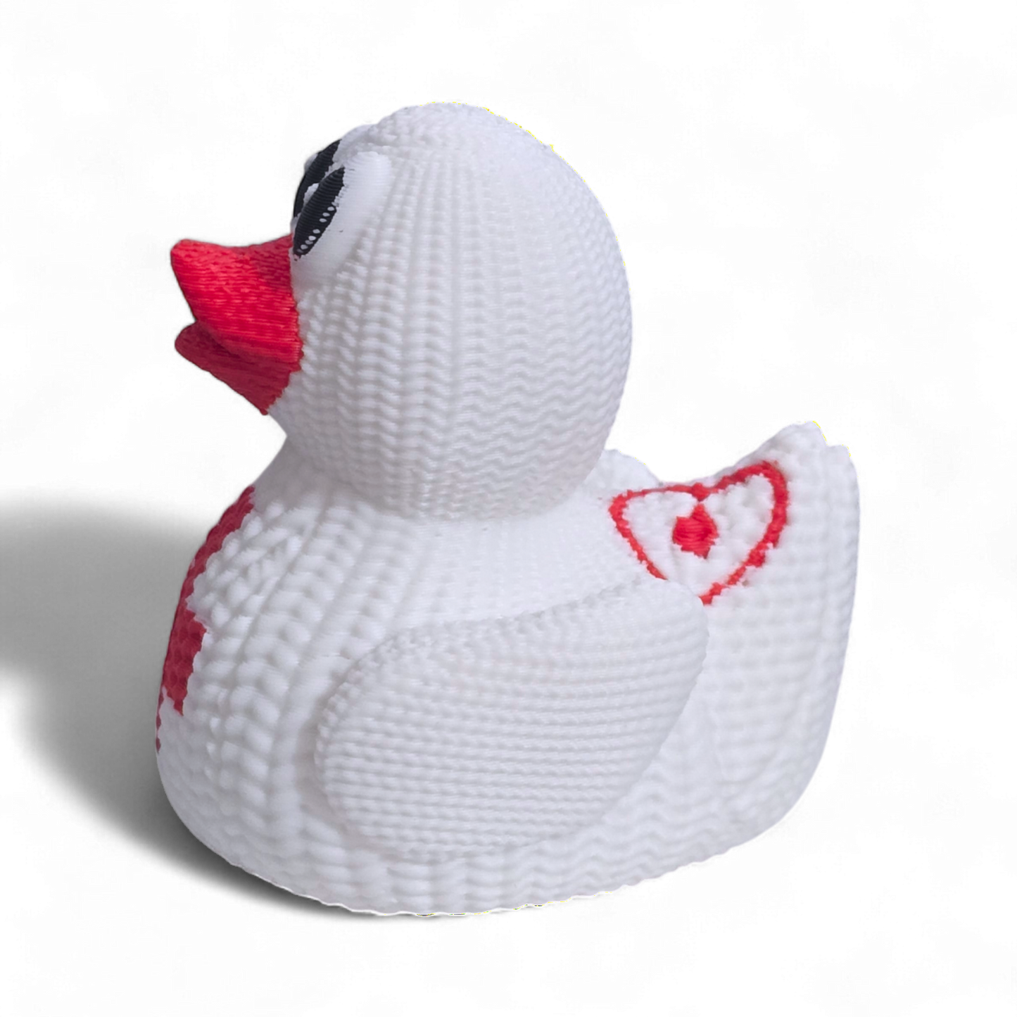 A white knitted 3D printed PLA duck with a red cross on its belly, a red beak, and black eyes, photographed on a white background with a soft shadow.