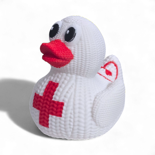 A white knitted 3D printed PLA duck with a red cross on its belly, a red beak, and black eyes, photographed on a white background with a soft shadow.