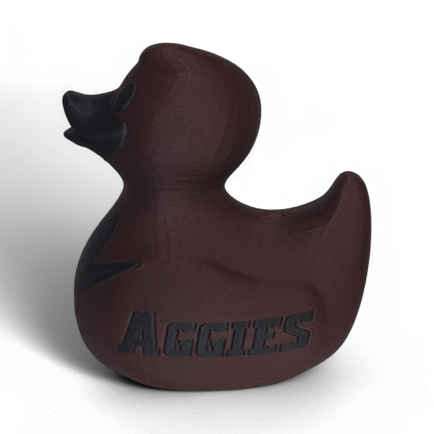 A dark brown 3D Printed PLA duck with a matte finish, featuring a black embossed cowboy hat logo and the word 'AGGIES' on the side, set against a plain white background.