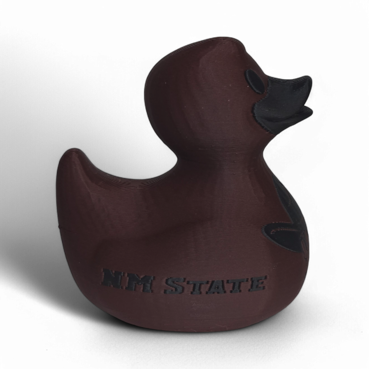 A dark brown 3D Printed PLA duck with a matte finish, featuring a black embossed cowboy hat logo and the word 'AGGIES' on the side, set against a plain white background.