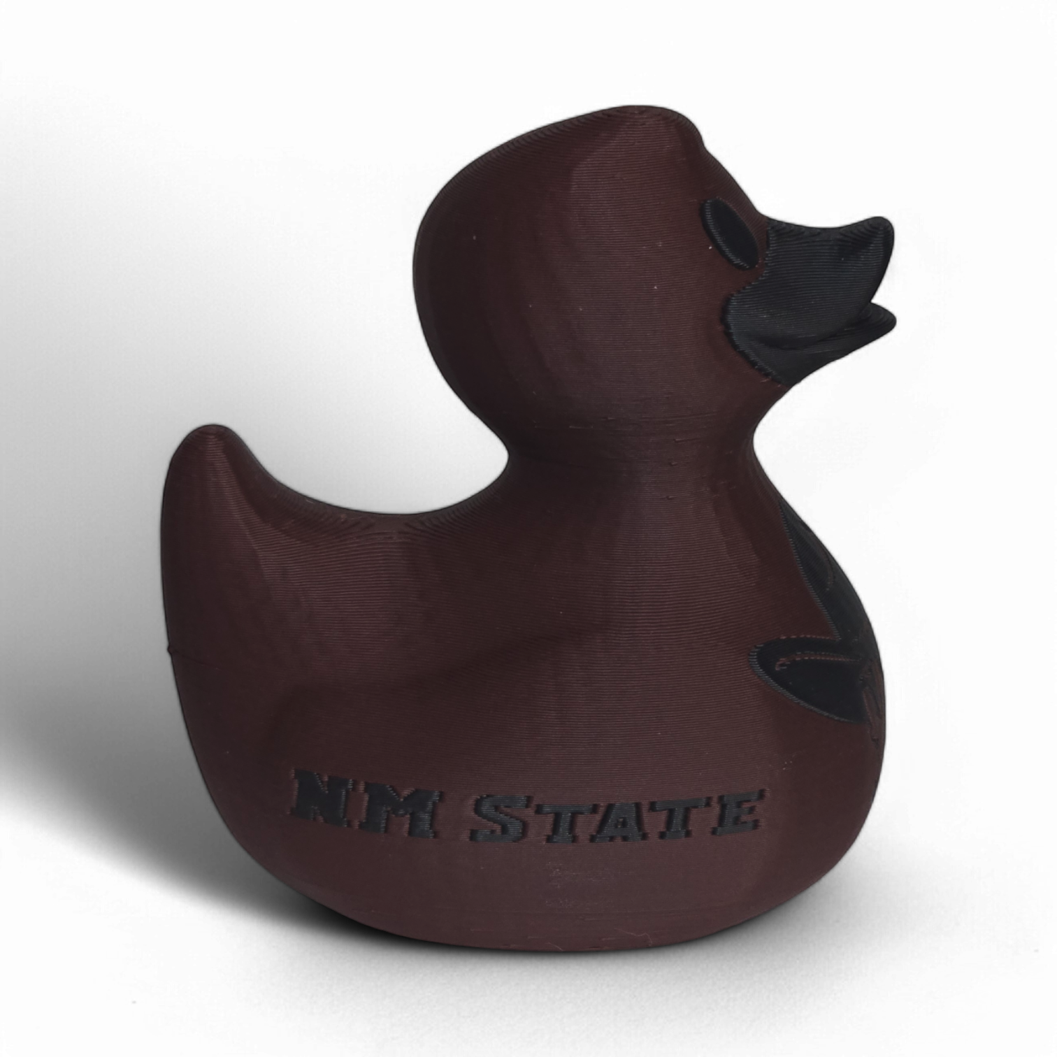 A dark brown 3D Printed PLA duck with a matte finish, featuring a black embossed cowboy hat logo and the word 'AGGIES' on the side, set against a plain white background.