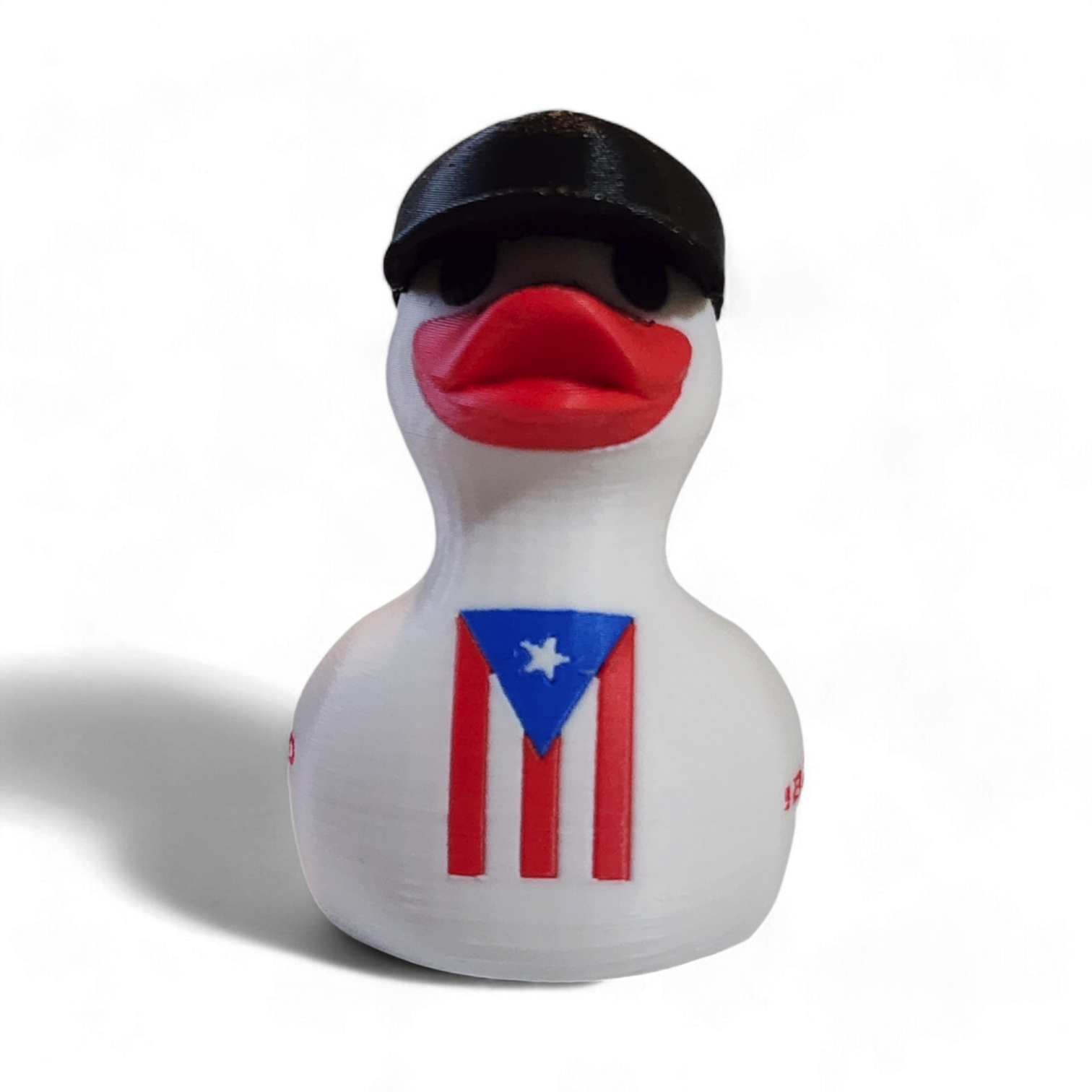 A white 3D printed duck wearing a black baseball cap with a white New Era logo, featuring a red beak and a Puerto Rico flag graphic on its side, with the red text '¡BENDITO' printed on the front.