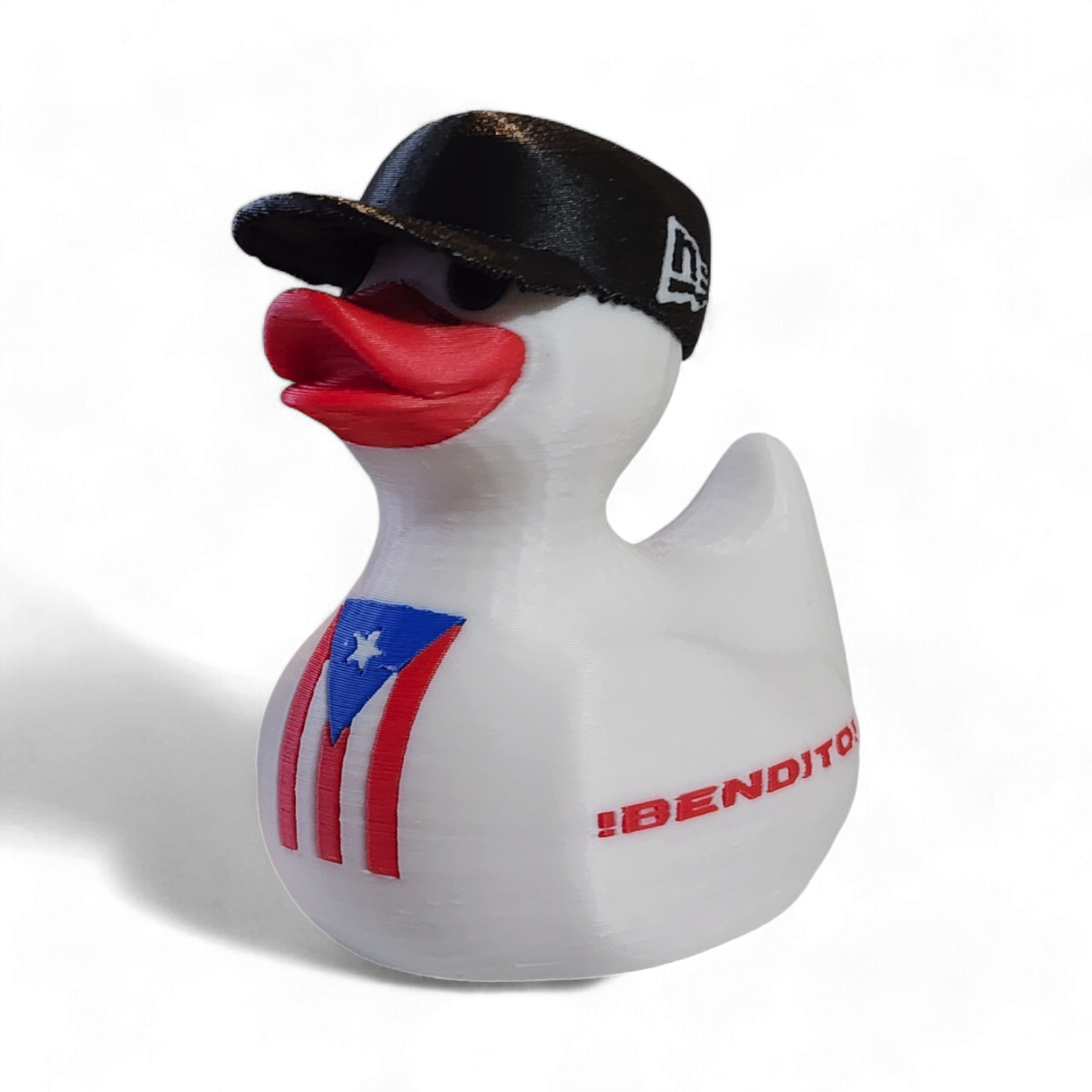 A white 3D printed duck wearing a black baseball cap with a white New Era logo, featuring a red beak and a Puerto Rico flag graphic on its side, with the red text '¡BENDITO' printed on the front.