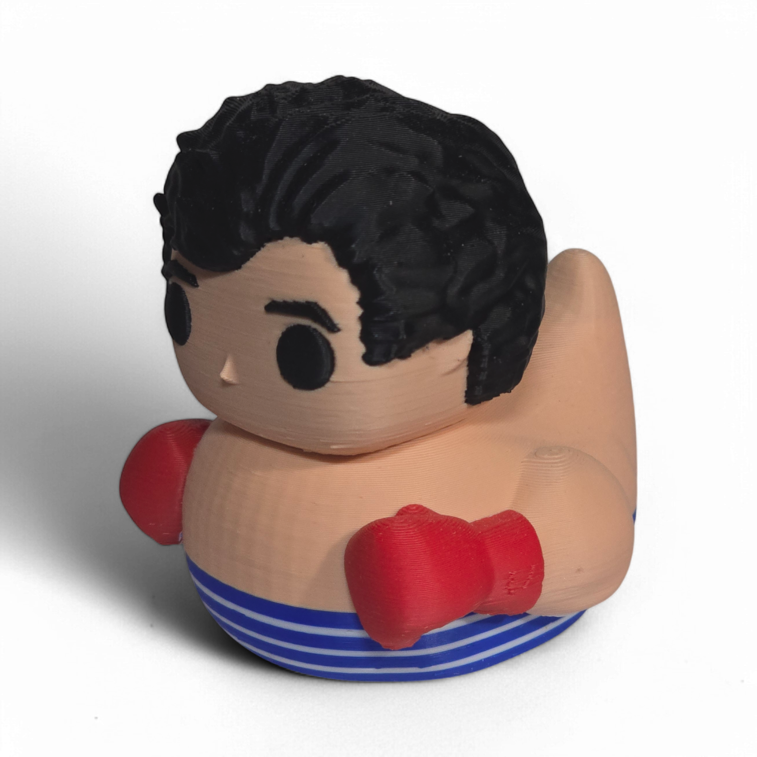 A novelty 3D Printed PLA duck shaped like a cartoon boy with black hair, a beige body, red boxing gloves, and blue-and-white striped shorts, photographed on a plain white background.