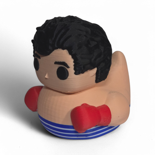 A novelty 3D Printed PLA duck shaped like a cartoon boy with black hair, a beige body, red boxing gloves, and blue-and-white striped shorts, photographed on a plain white background.