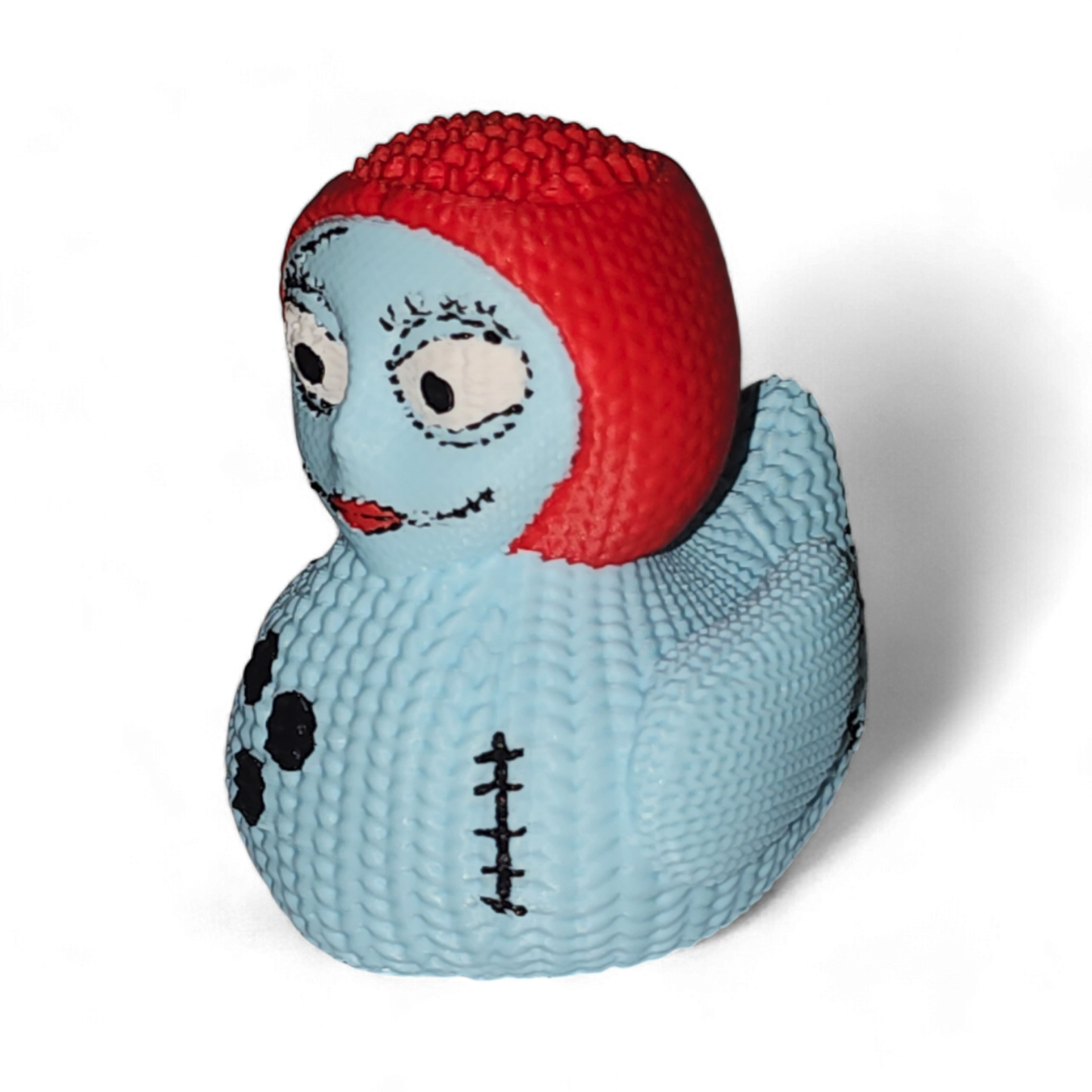 A 3D Printed PLA duck, featuring a light blue body with black spots and a stitched seam, topped with a bright red textured head resembling hair, and detailed with cartoon eyes and a smile.