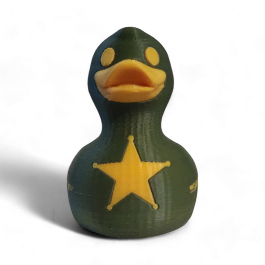 A 3D-printed 3D printed PLA duck styled as a sheriff's deputy, featuring an olive green body, a yellow beak and eye, a yellow sheriff's star badge on its side, and the word 'SHERIFF' printed in yellow.