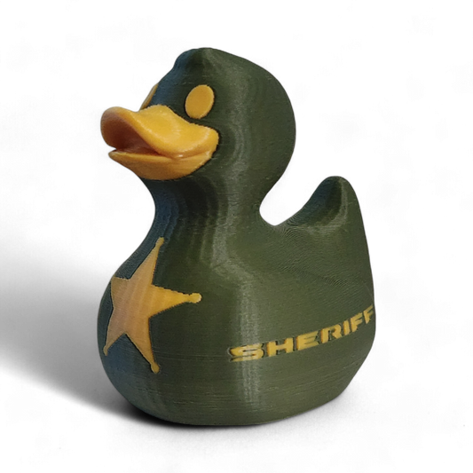 A 3D-printed 3D printed PLA duck styled as a sheriff's deputy, featuring an olive green body, a yellow beak and eye, a yellow sheriff's star badge on its side, and the word 'SHERIFF' printed in yellow.