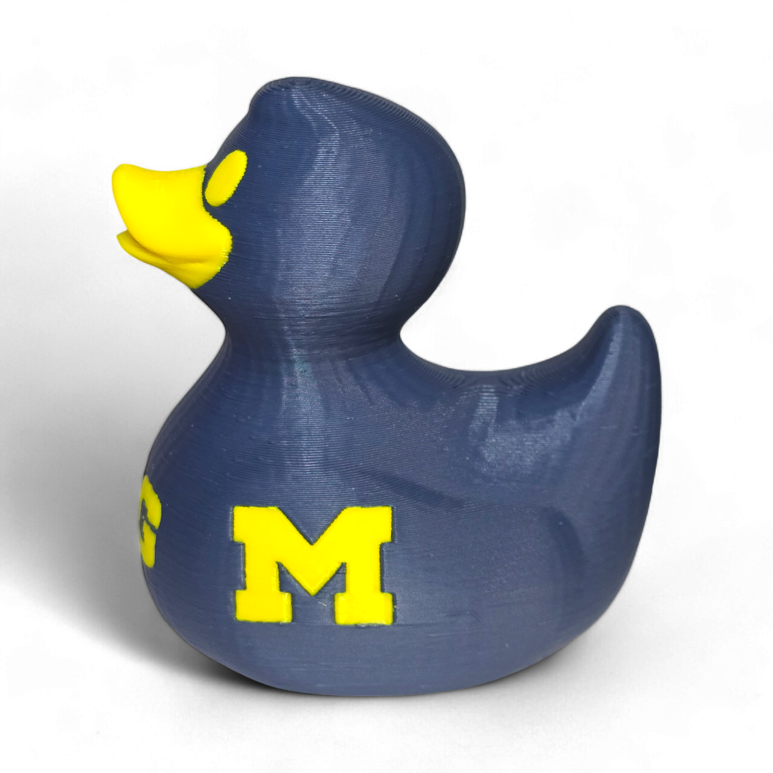 A 3D-printed PLA duck in navy blue with a bright yellow beak and a large yellow letter 'M' on the side, representing the Michigan Wolverines, on a white background.