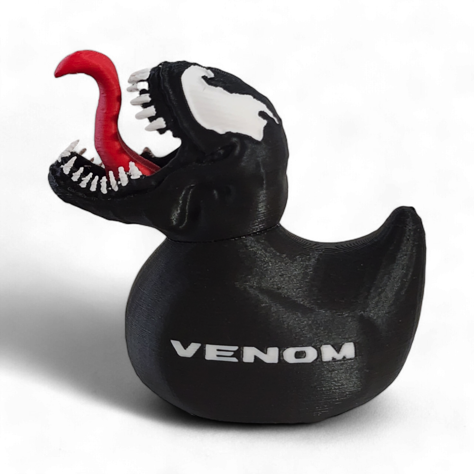 A black 3D Printed PLA duck with a Venom-themed design, featuring a red tongue sticking out, white teeth, a white and black pattern on the head, and the word 'VENOM' printed in white on the side.